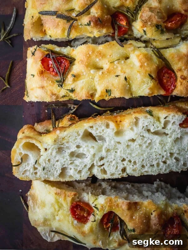 How to Make No-Knead White Bread at Home 12 Slices of tomato focaccia on a wooden cutting board showing the crumb cross section.
