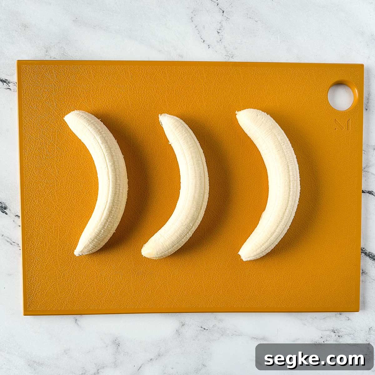 Three peeled bananas on a yellow cutting board.