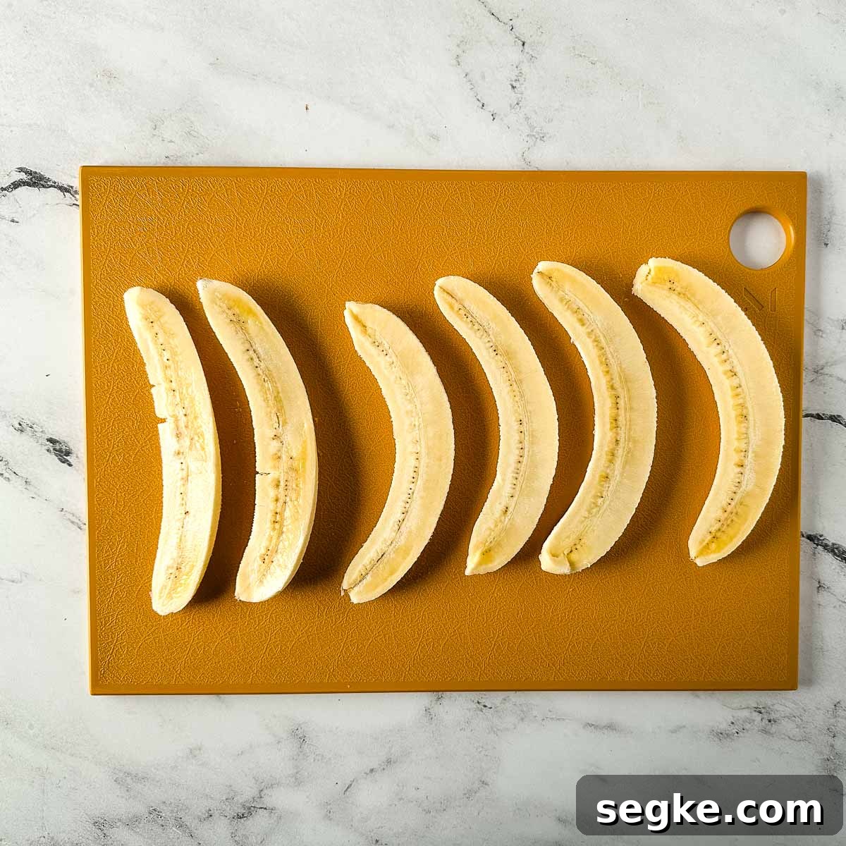 Halved bananas sit on a yellow cutting board.