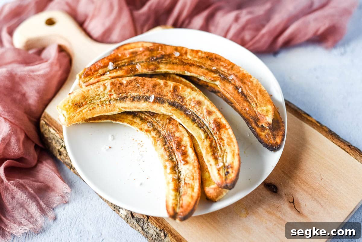 A pinch of flakey sea salt is added to the air fryer bananas sitting on a white plate.