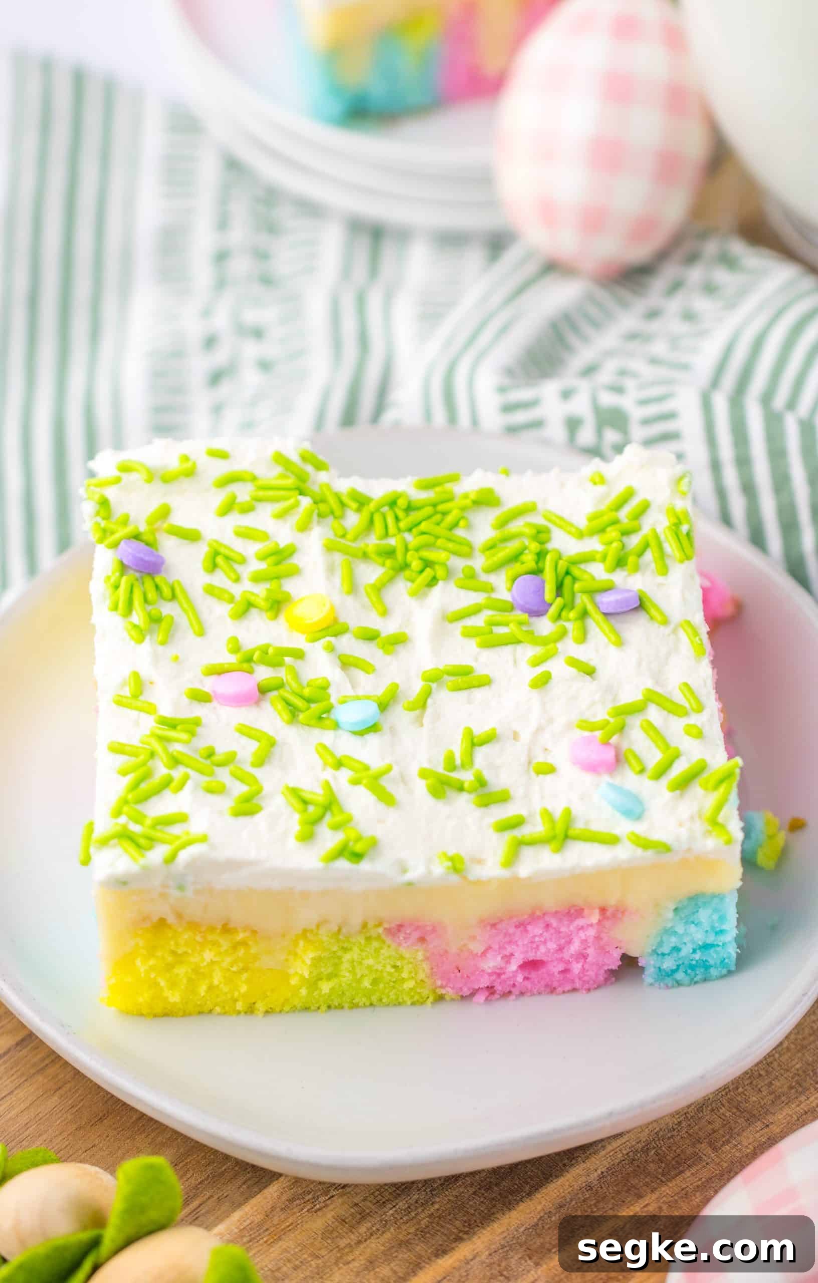 a slice of pastel rainbow colored easter poke cake on a small white dessert plate with a glass of milk in the background