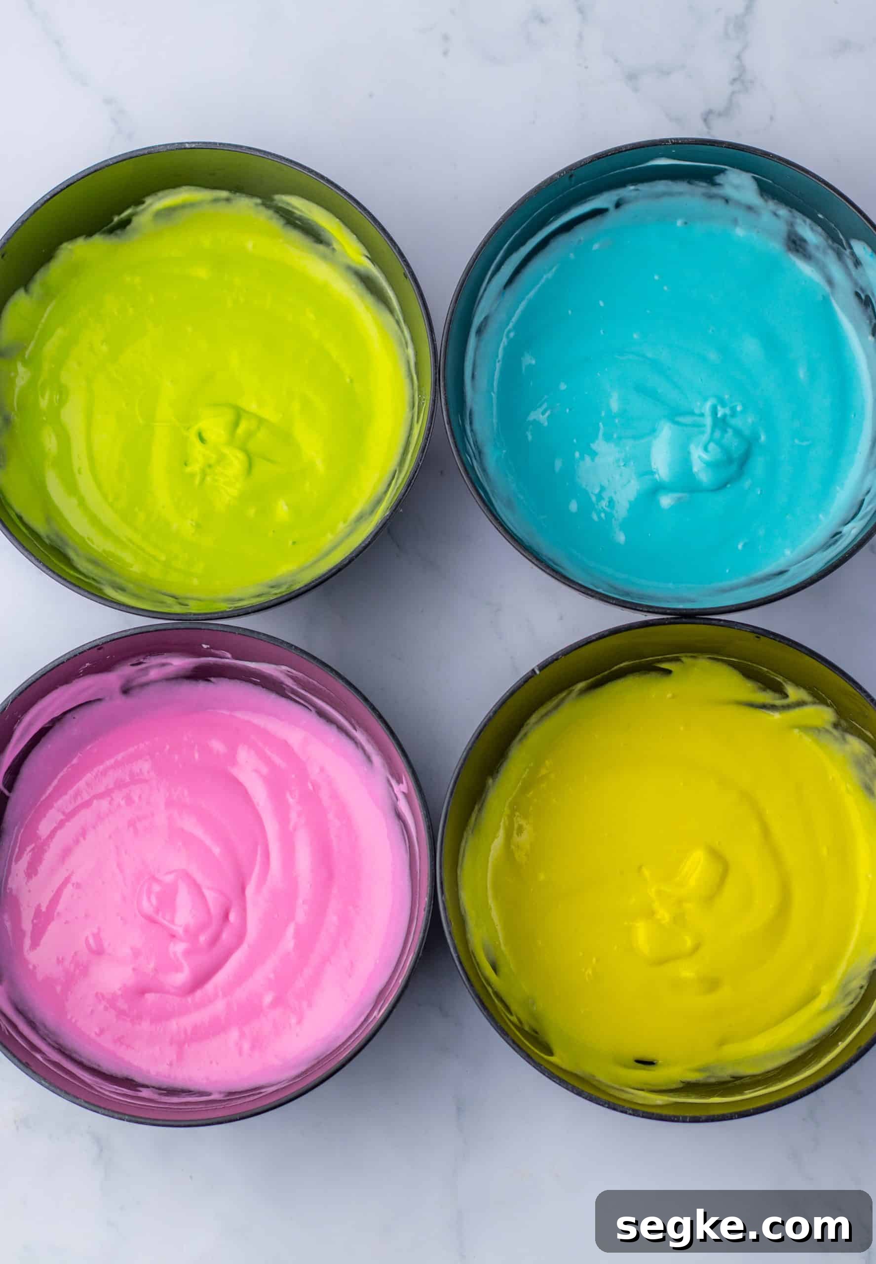 four cake pans filled with different pastel colors of cake batter