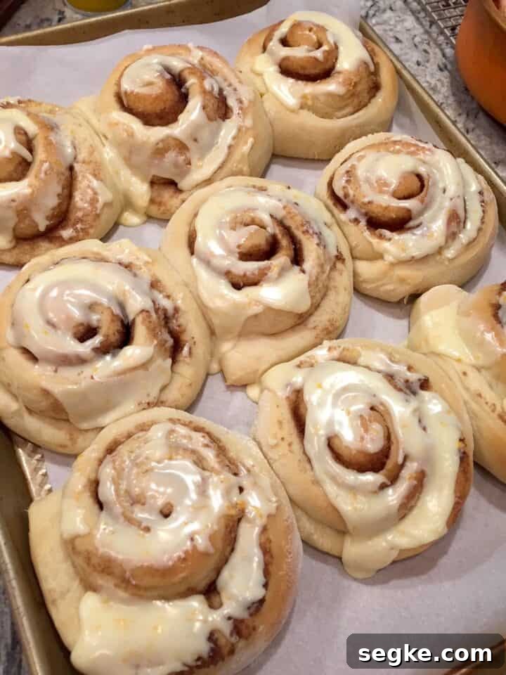 Orange rolls with icing on parchment paper on a baking sheet.