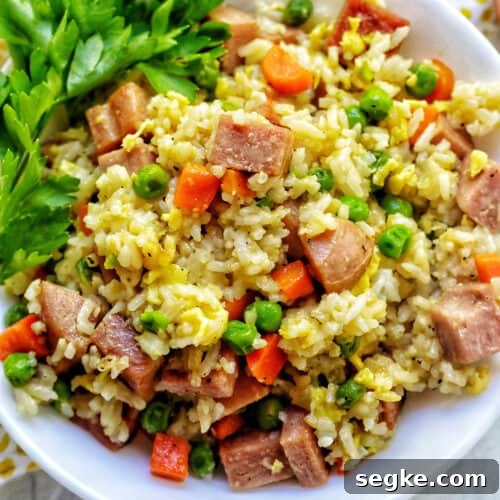 spam fried rice with peas, carrots, and parsley garnish in a white bowl.