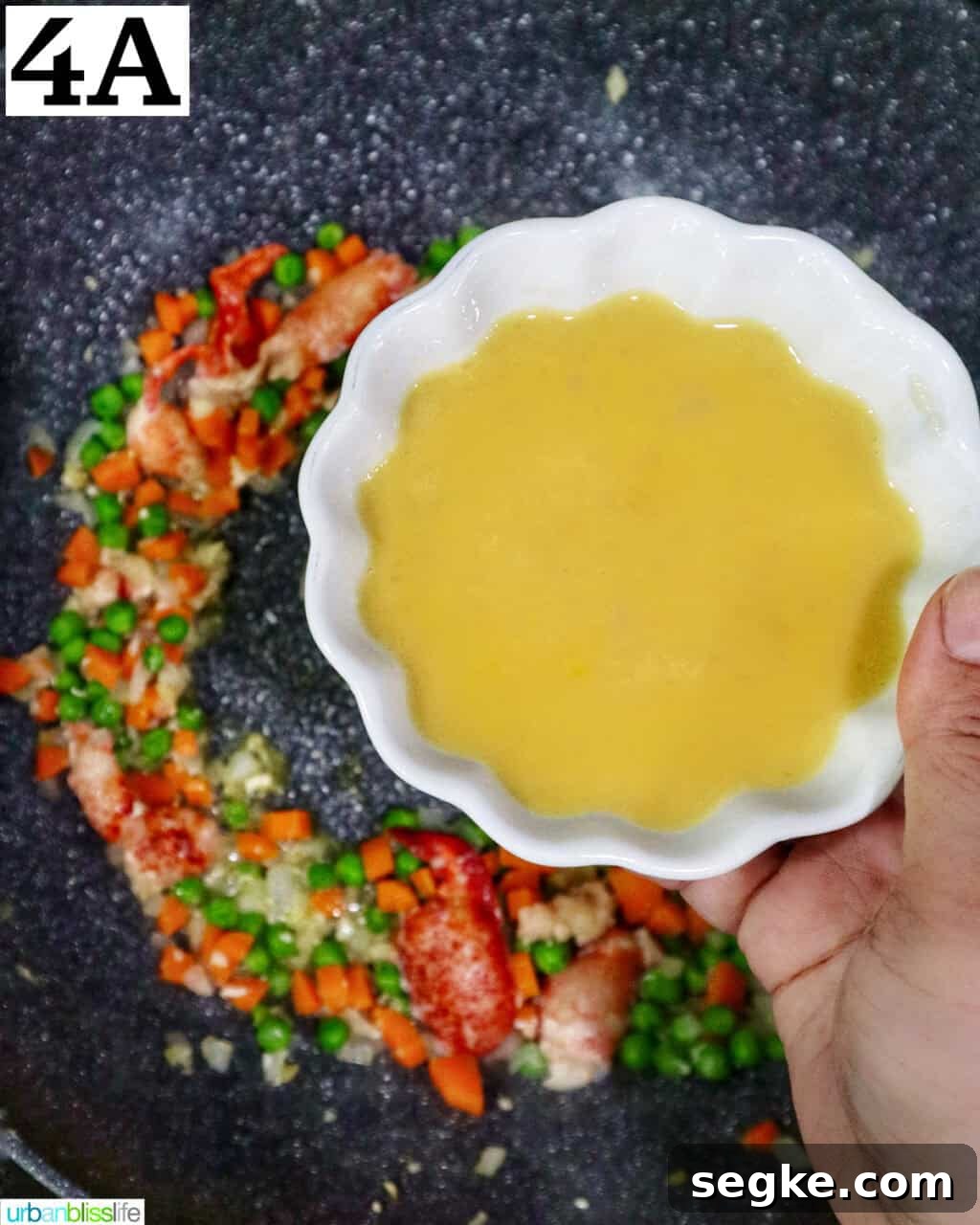 Garlic Butter Lobster Fried Rice 10 hand holding a bowl of beaten eggs over a wok with fried rice.
