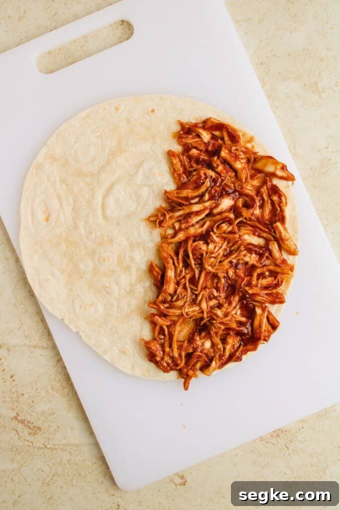 Smoky BBQ Chicken Quesadillas with Melted Cheese 6 Meat being layered on top of a tortilla.