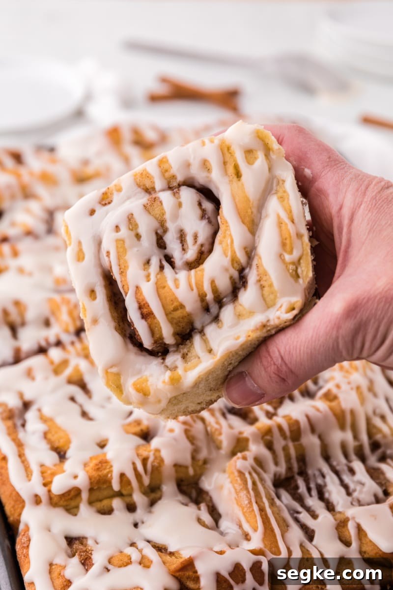 Pulling a cinnamon roll from the pan hand pulling cinnamon roll out of pan of cinnamon rolls