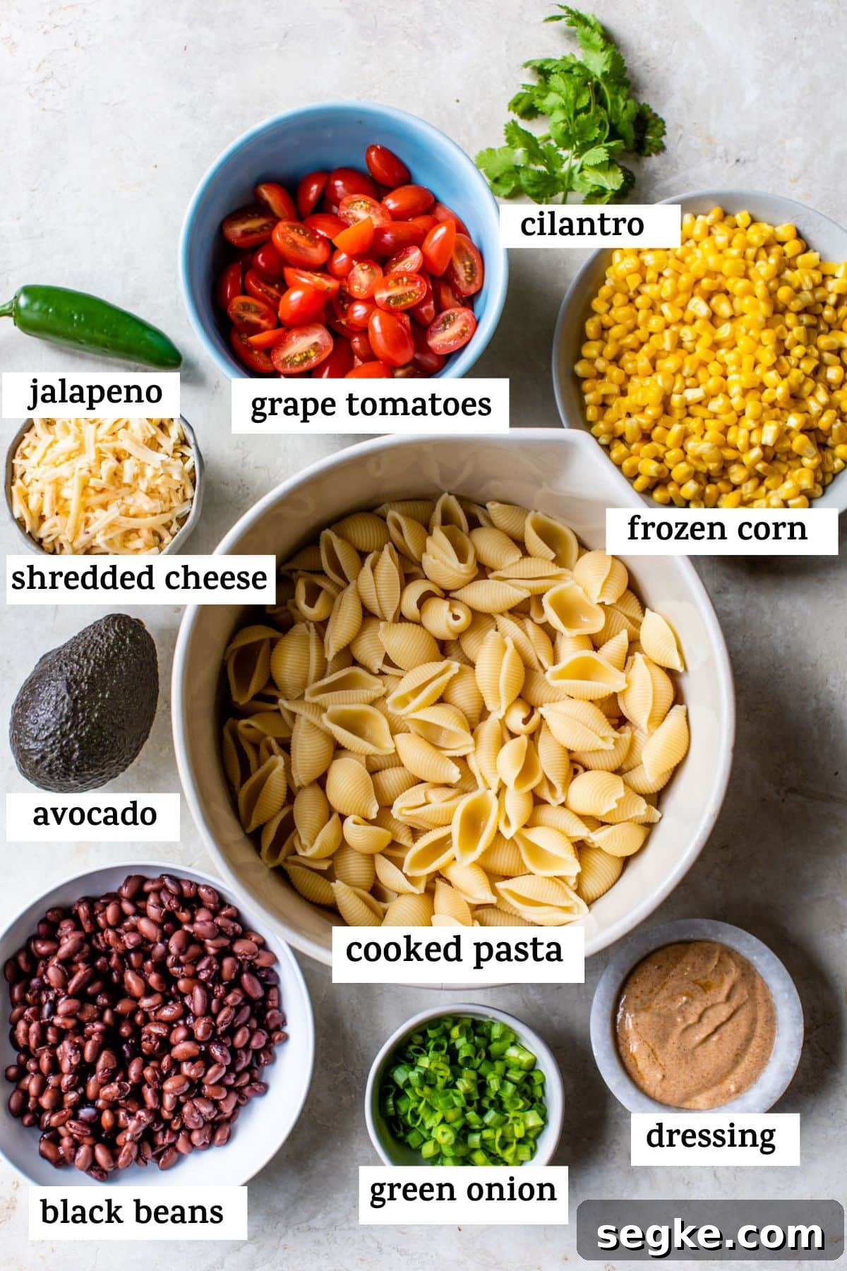Southwest Taco Pasta Salad Recipe 2 a list of all of the ingredients in the taco pasta salad: jalapeno, grape tomatoes, cilantro, frozen corn, shredded cheese, avocado, cooked pasta, black beans, green onion, and dressing