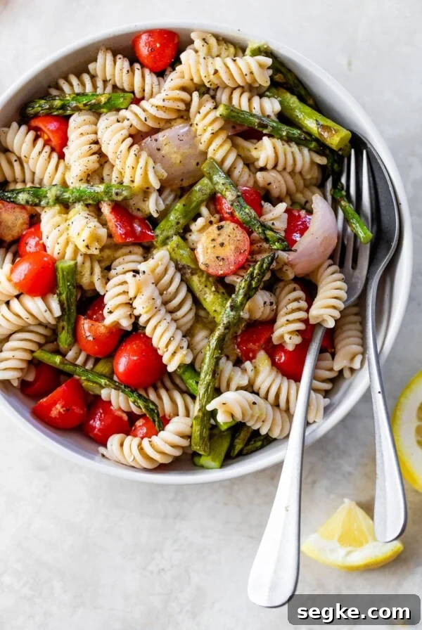 rotini pasta in a white bowl with chopped asparagus, tomatoes and red onion