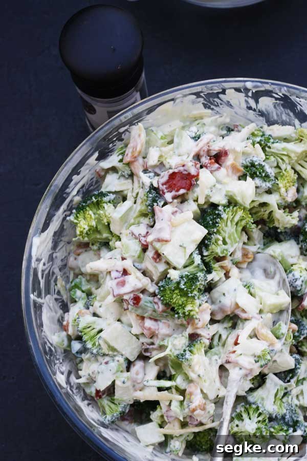 Overhead view of the edge of a glass bowl with broccoli, apple and bacon salad in it.