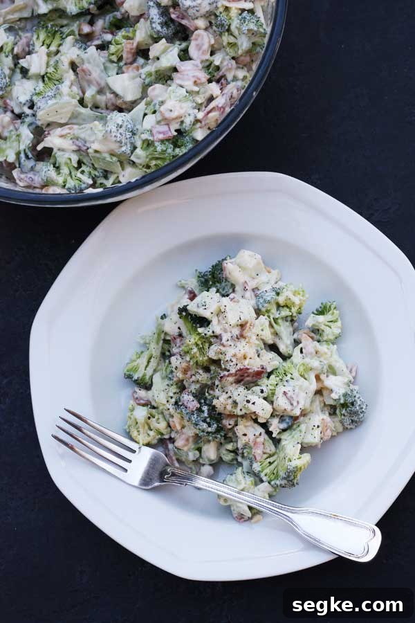 Broccoli, bacon and apple salad in a white bowl with a fork on a black background.