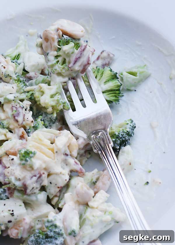 Closeup of a fork on a white plate of broccoli, bacon and apple salad.