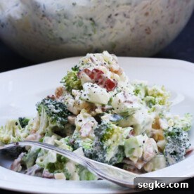 A white bowl with broccoli, bacon and apple salad with a spoon in the front and a glass bowl with more salad behind.
