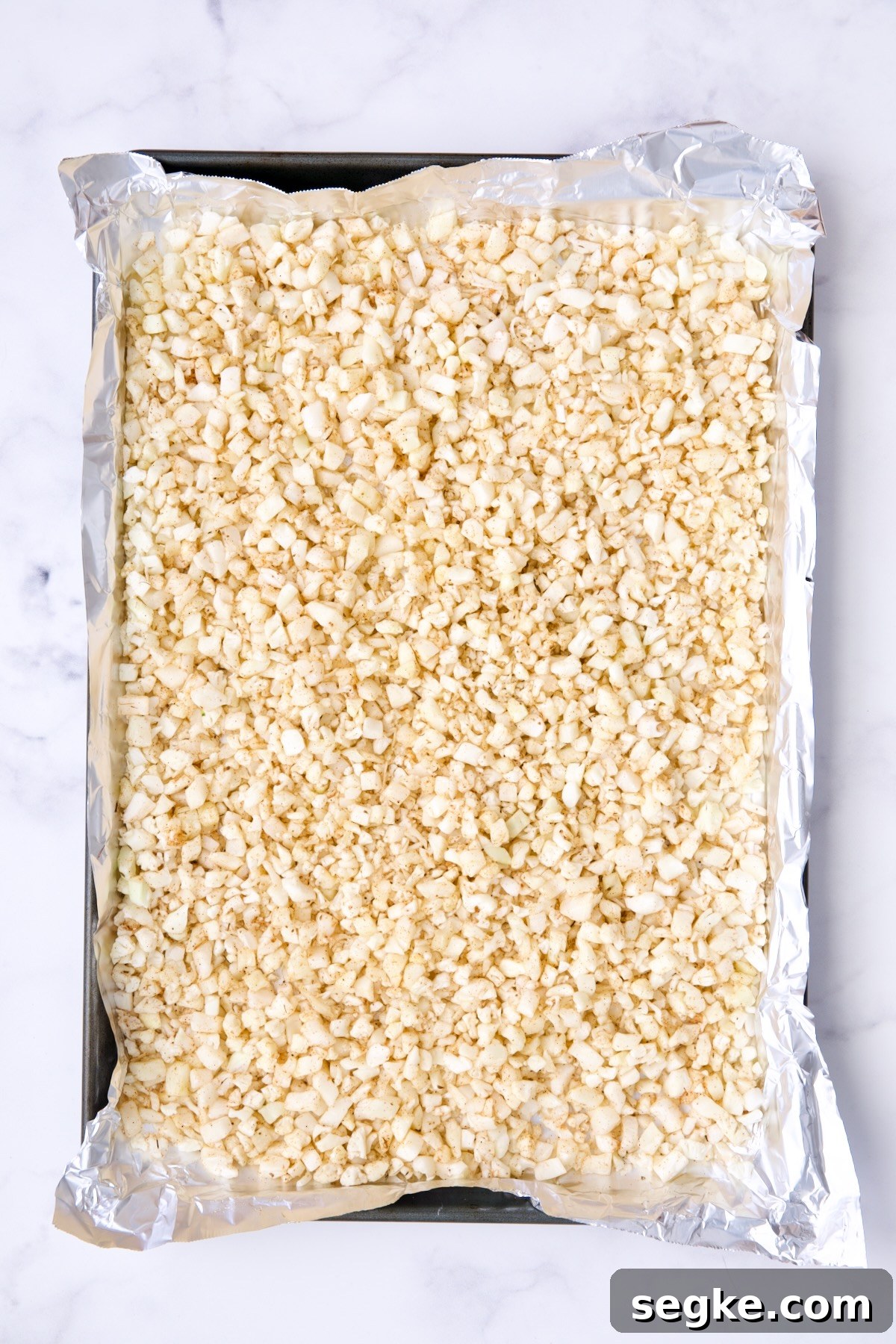 Uncooked riced cauliflower on aluminum foil-lined baking sheet.