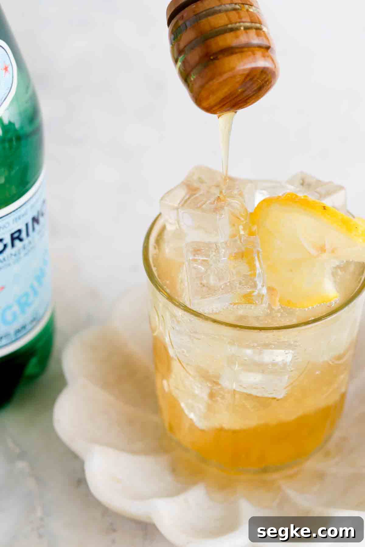 Honey dripping into a glass of a ginger mocktail with a green bottle of sparkling water next to it.