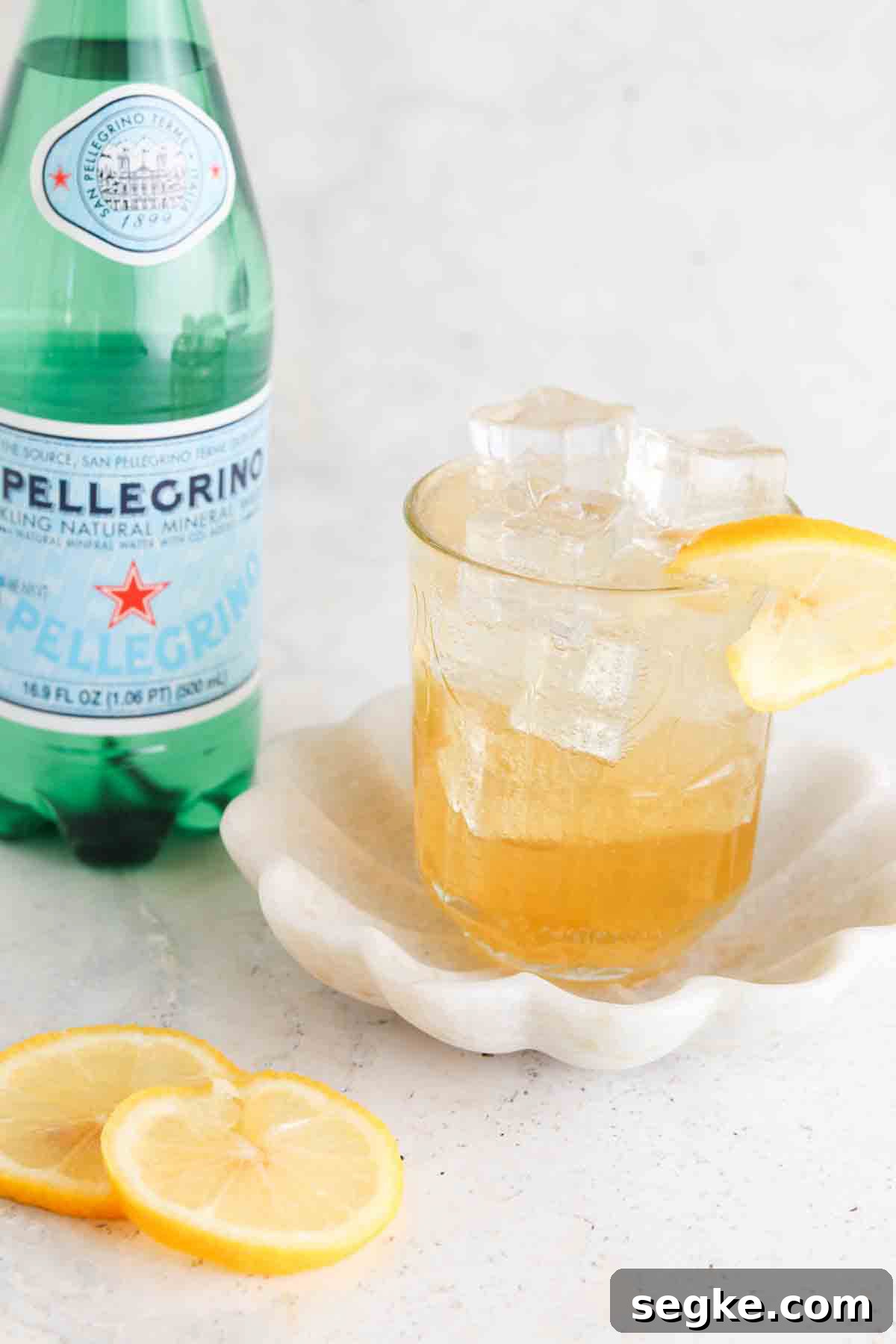 Ginger mocktail in a glass with a lemon on top and a bottle of sparkling water sitting next to it.