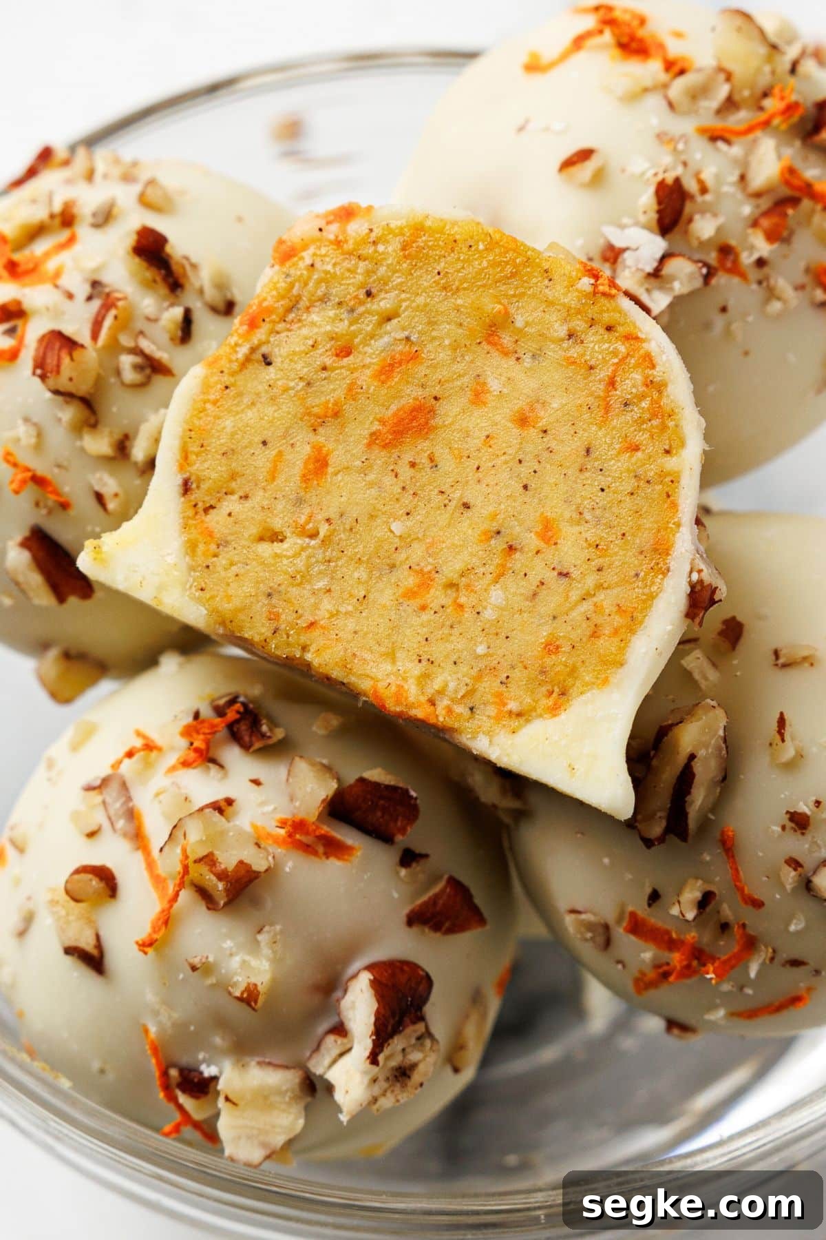 No Bake Keto Carrot Cake Protein Bites 2 Keto carrot cake bites coated in white chocolate with pecans and shredded carrots, one bitten in half to show the spiced inside