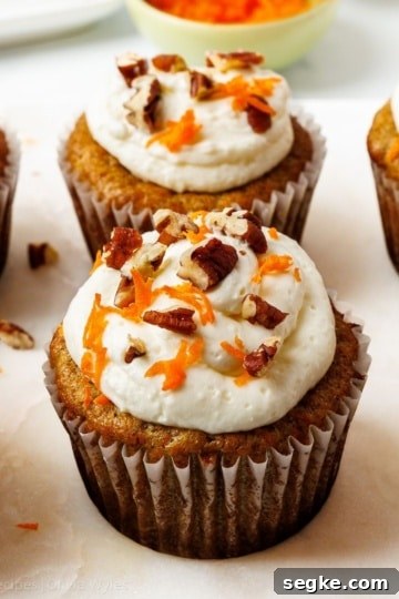 Six frosted carrot cake cupcakes topped with cream cheese frosting, chopped pecans, and finely grated carrots