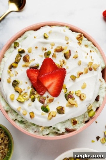 Overhead view of pistachio fluff in a pink ceramic bowl with strawberry slices, pistachios, and whipped cream garnish