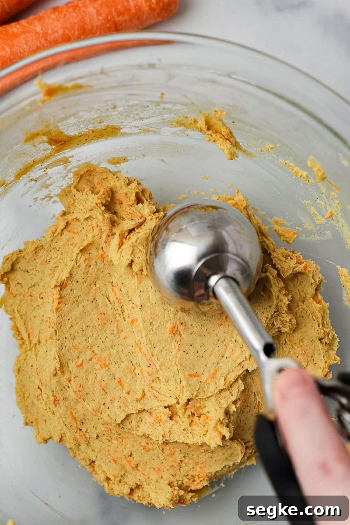 No Bake Keto Carrot Cake Protein Bites 6 Cookie scoop portioning the carrot cake bite mixture from a glass bowl