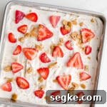 An icebox cake in a baking pan topped with strawberries and graham cracker crumbs.