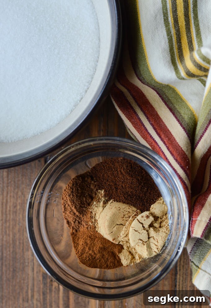 A bowl of sugar next to a bowl with cinnamon, nutmeg, cloves and ginger. Both are sitting next to a striped napkin.
