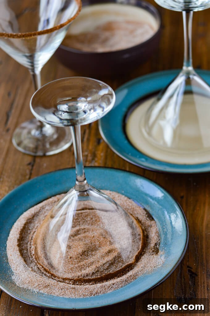 Two plates one with water and a martini glass dipped in it. Another one with pumpkin spice sugar and a martini glass dipped in it. One martini glass sitting upright with spiced sugar on its rim.