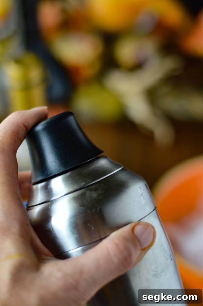 A cocktail shaker in a hand with fall decorations in the background.