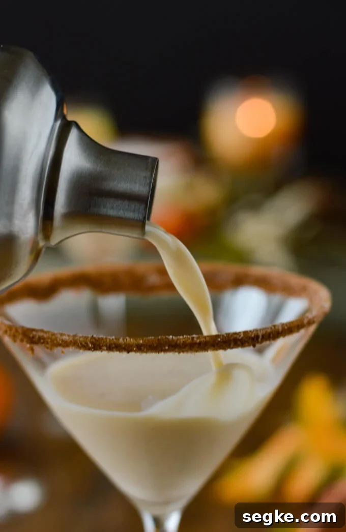Pouring a pumpkin spice martini from a cocktail shaker into a martini glass with spiced sugar on its rim.