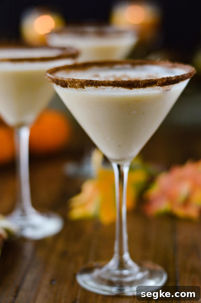 Three pumpkin spice martinis with spiced sugar on the rims and fall decorations around.