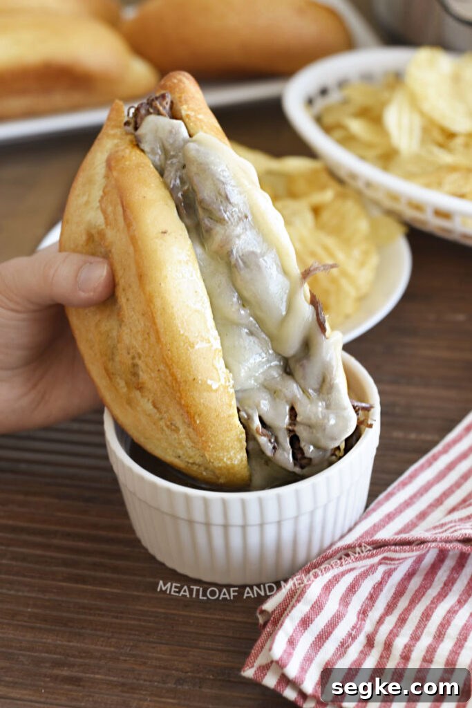 dip french dip sandwich made with beef chuck roast and melted provolone cheese in au jus gravy in white ramekin