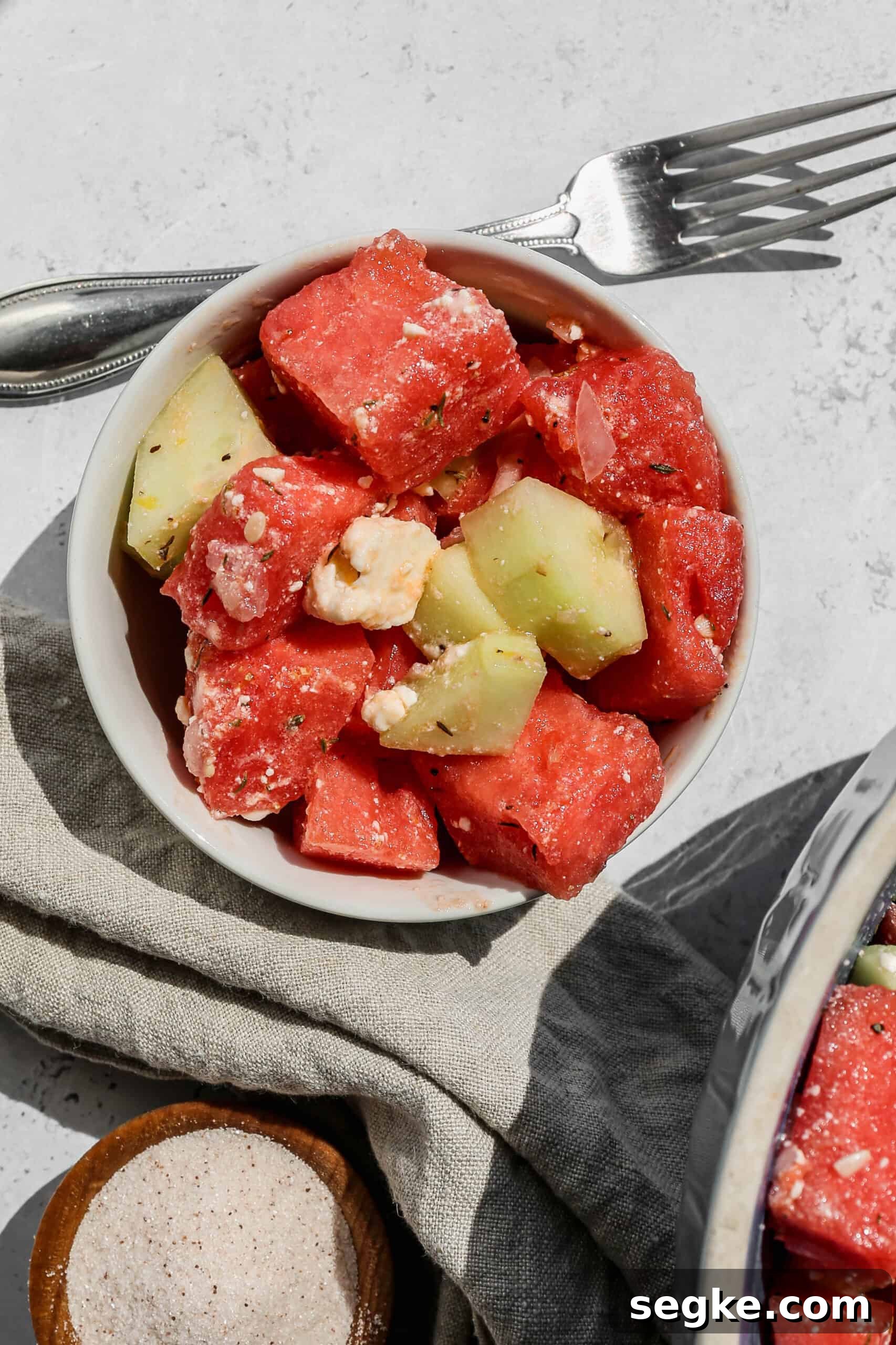 Refreshing Watermelon, Cucumber and Feta Salad Recipe 2 a small white bowl of watermelon cucumber feta salad next to a small wooden bowl of salt.