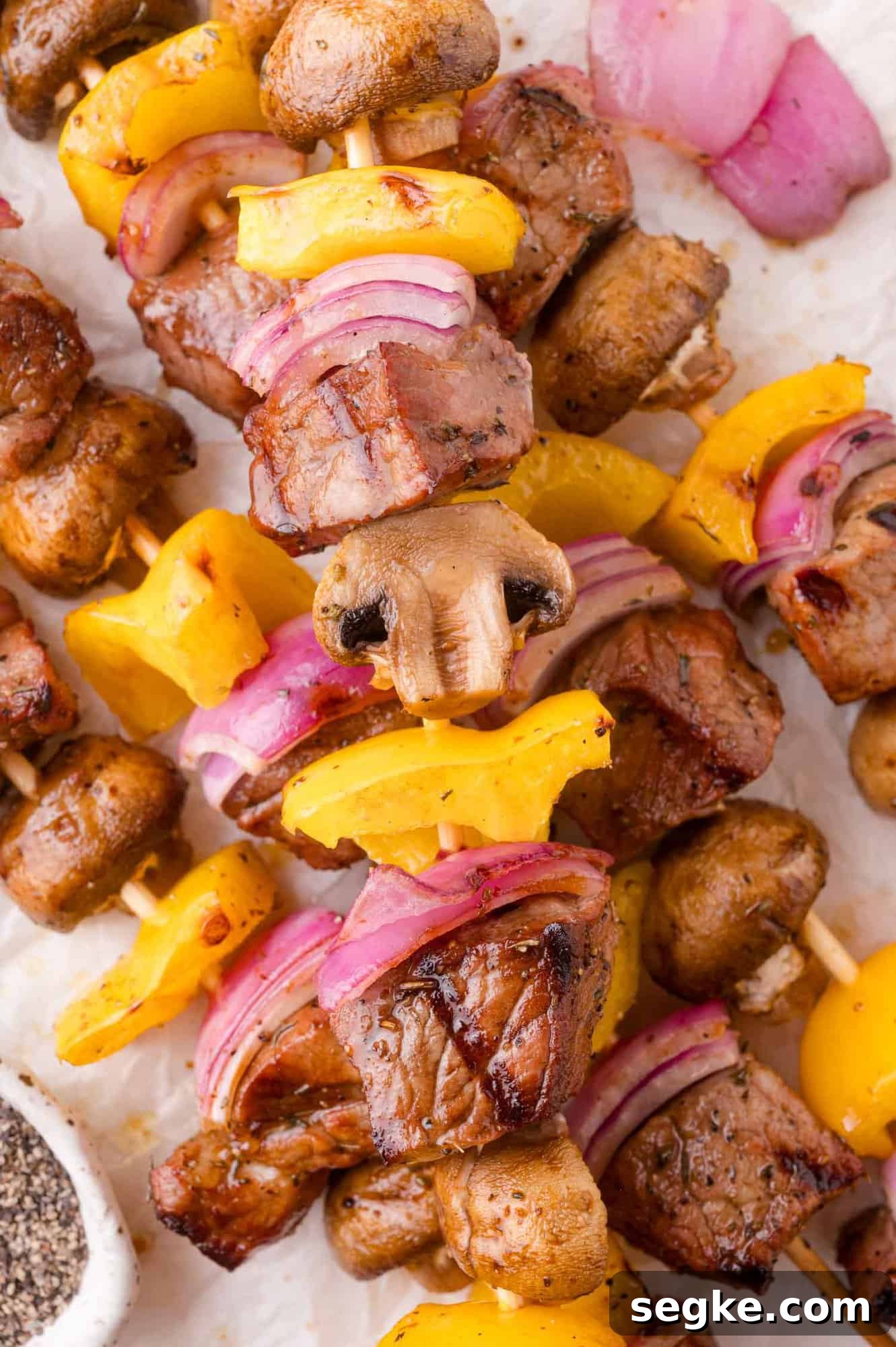 Marinated Steak Kabobs with Garlic and Herbs 2 Grilled skewers with chunks of steak, yellow bell peppers, red onions, and mushrooms arranged on a white surface.