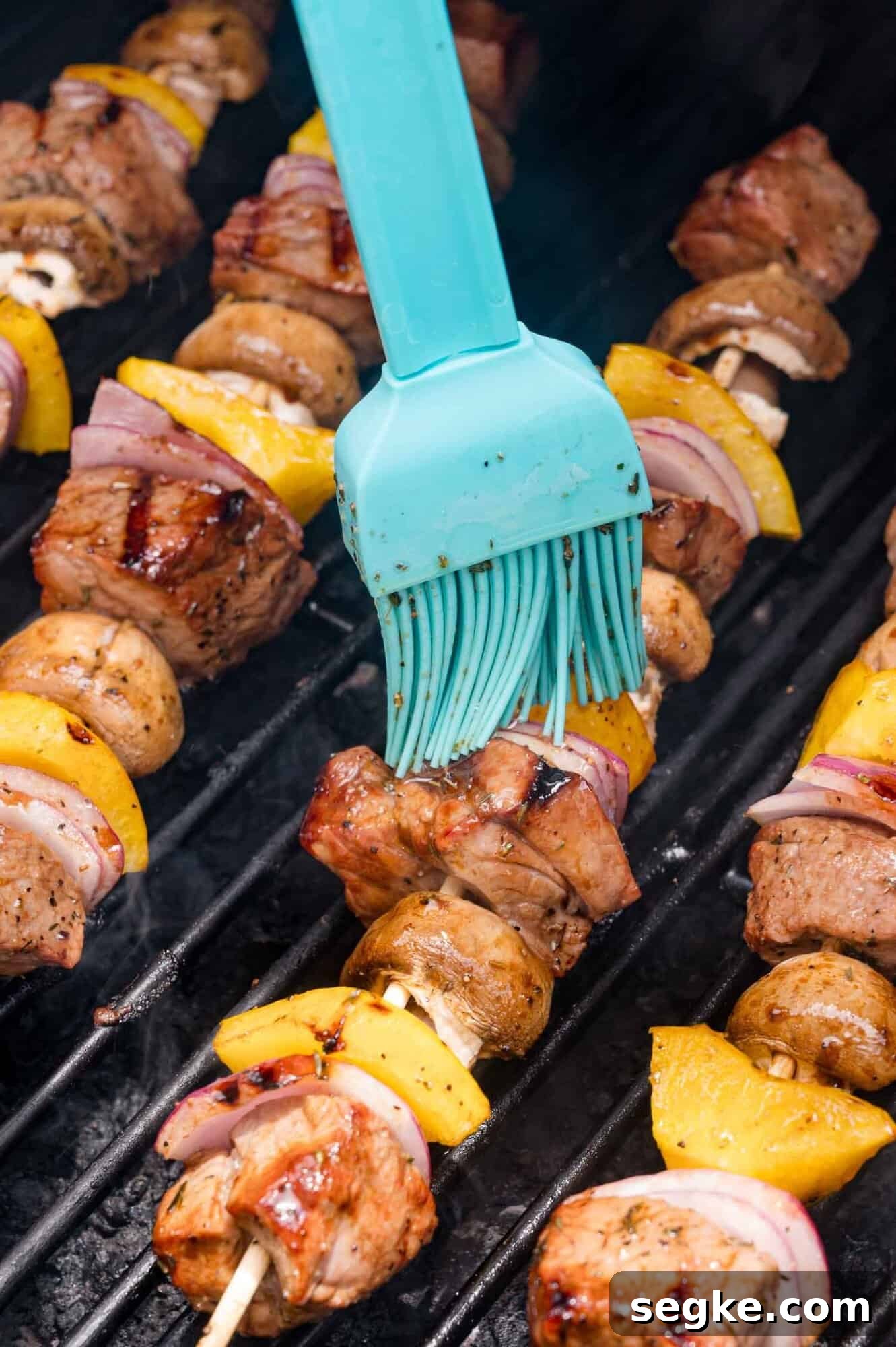 Marinated Steak Kabobs with Garlic and Herbs 6 A silicone brush applies marinade to meat and vegetable skewers grilling on a barbecue.