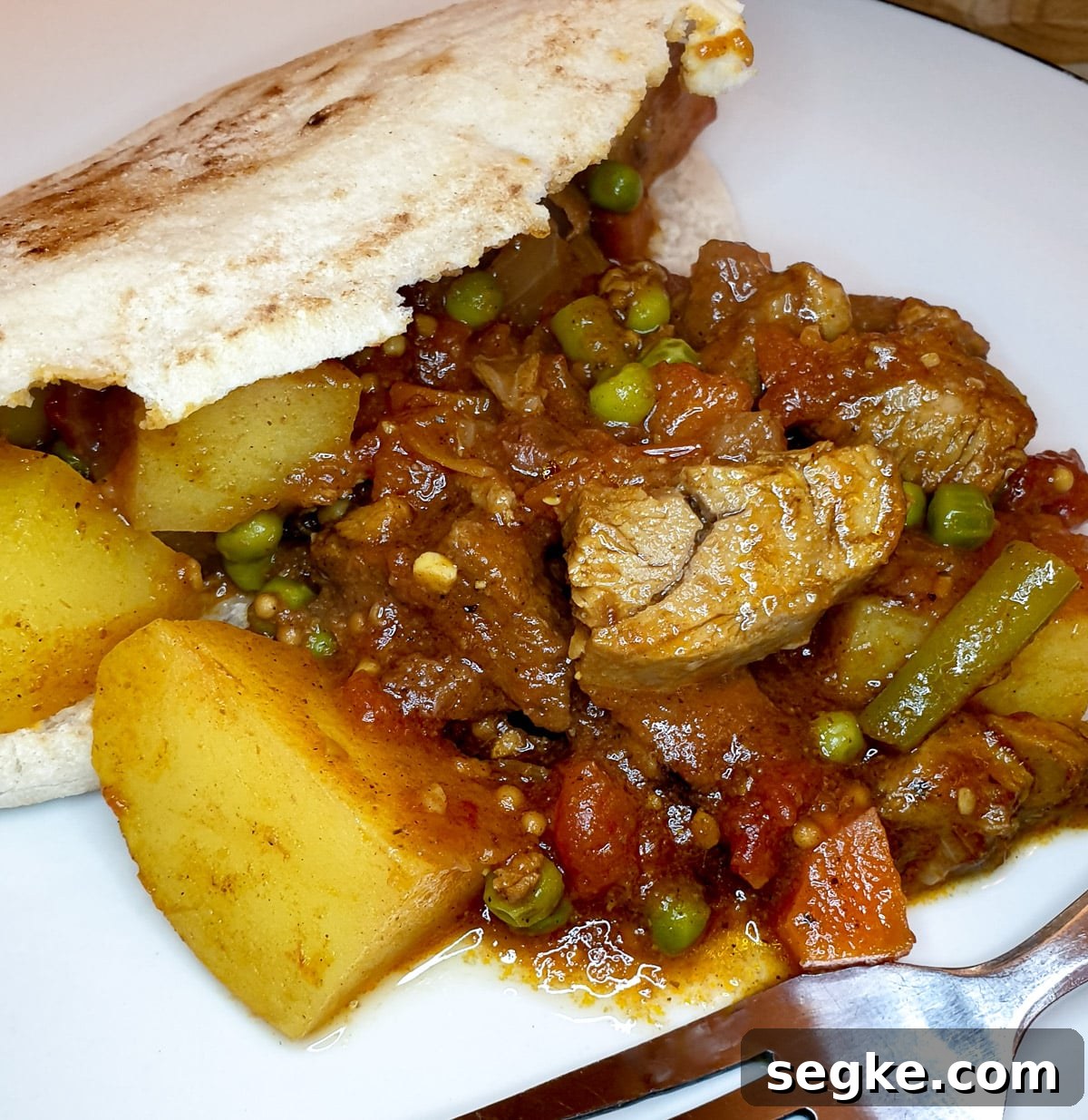 Leftover lamb curry in pita bread on a white plate.