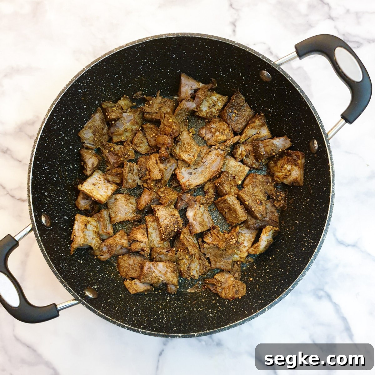 Cubes of lamb coated with spices in a frying pan.