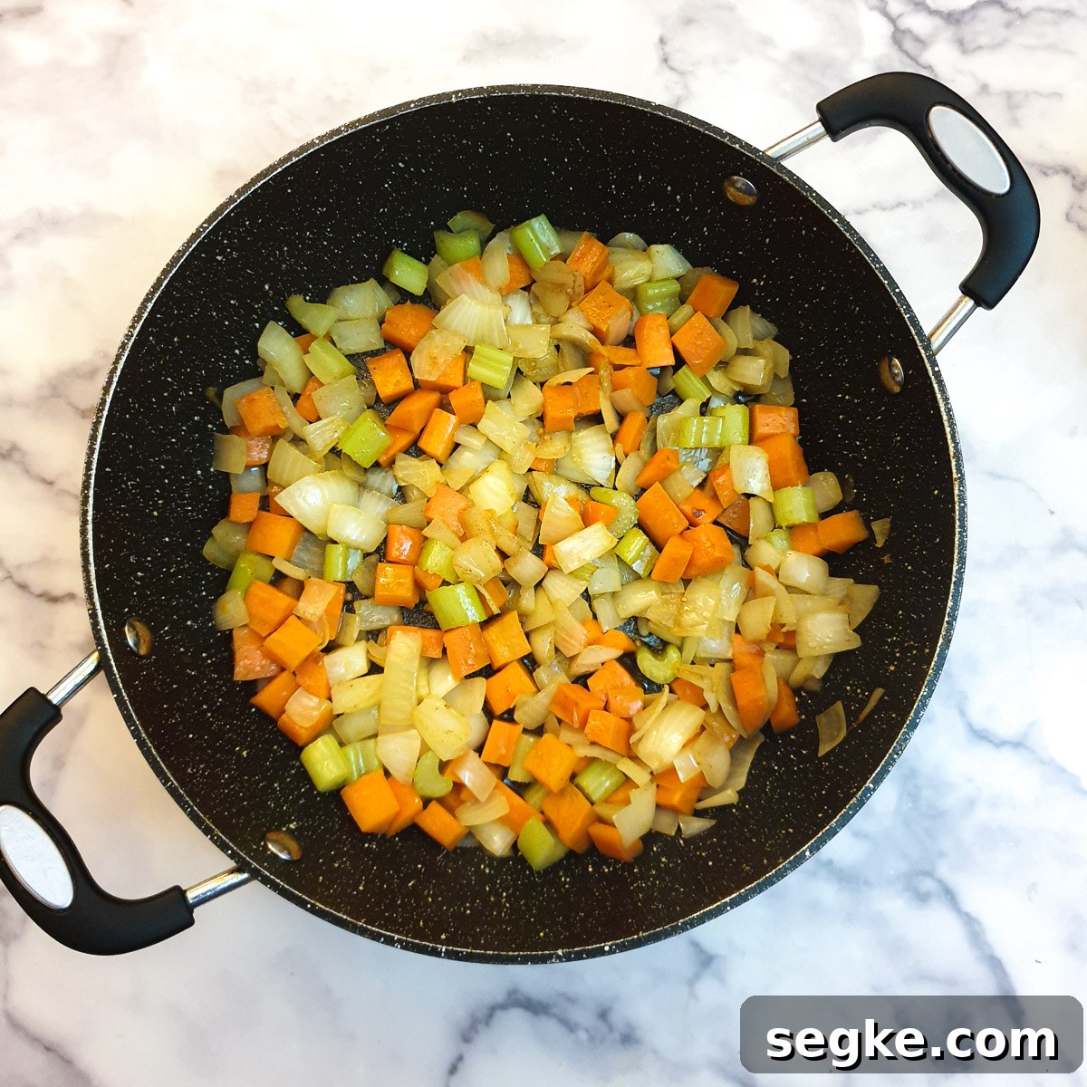 Carrots, onions and celery pieces frying in a frying pan.
