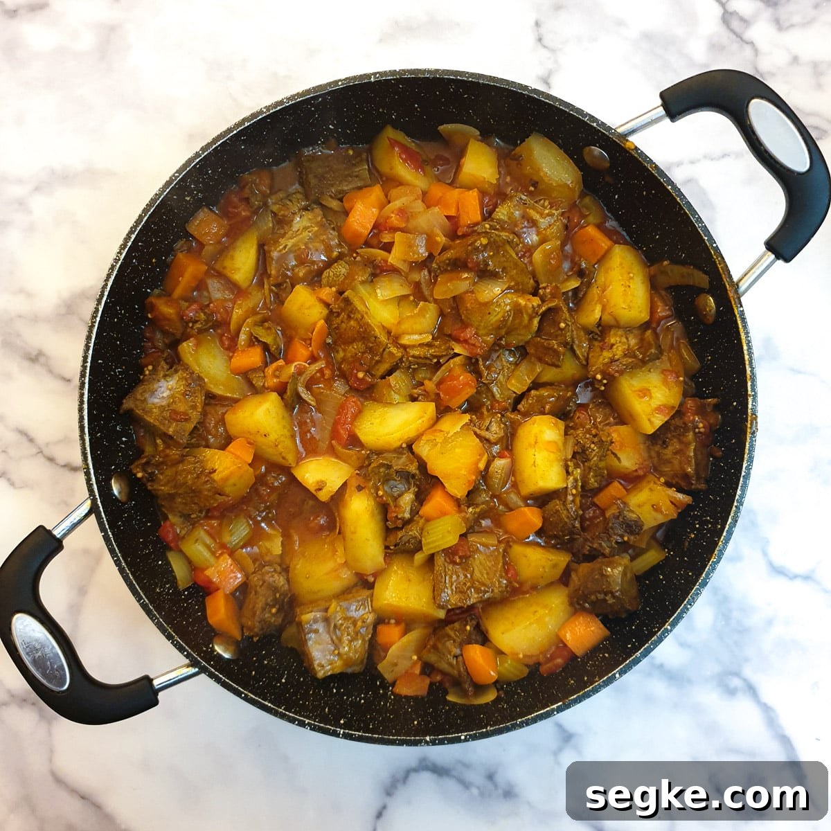 Cubed lamb added to curry sauce in a frying pan.