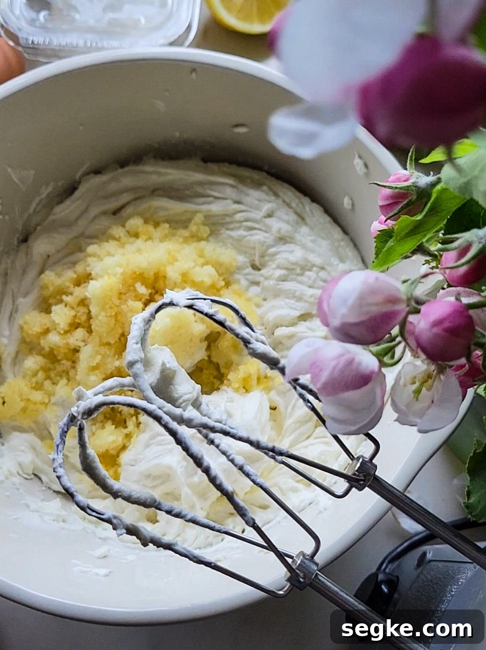 Lemon cheesecake batter in a bowl with lemon sugar sitting on top, the beaters of a handheld mixer in the foreground