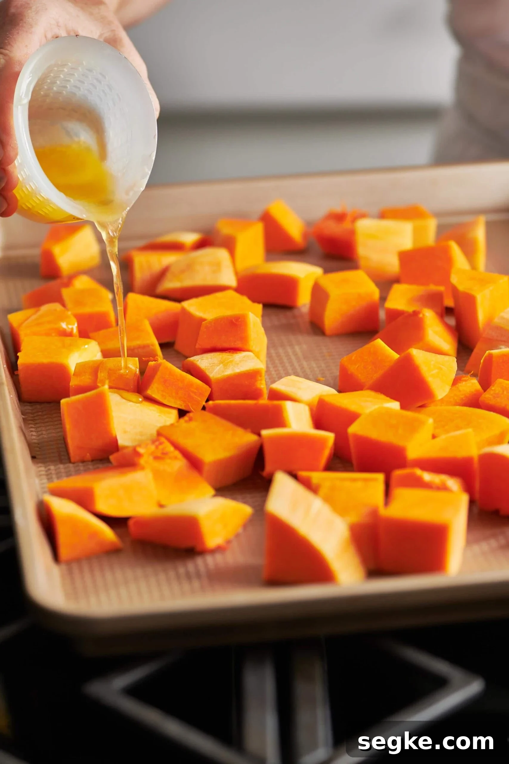 Woman pouring melted butter over cubes of Butternut Squash.