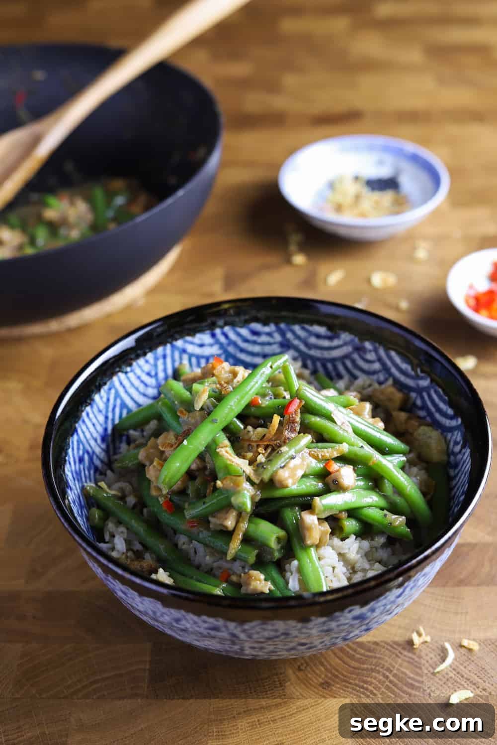 Photo of a bowl of vegan chinese green beans with tempeh and pan in the background