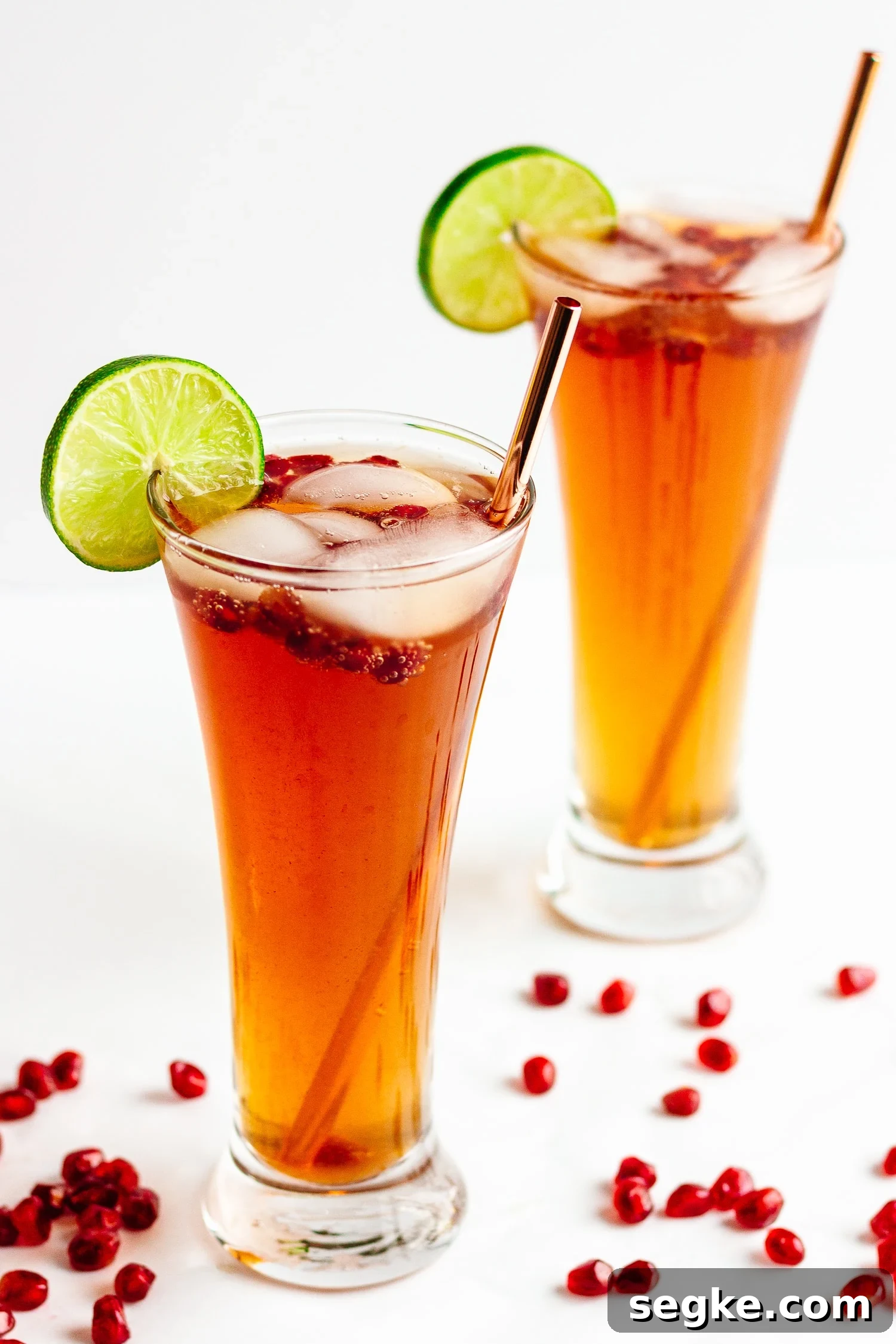 Sparkling Pomegranate Lime Spritzer Recipe 2 Two glasses of pomegranate lime spritzer on a white background with pomegranate arils sprinkled around