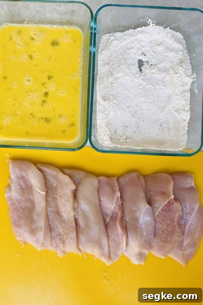 Chicken cutlets with beaten eggs, and flour on a counter.