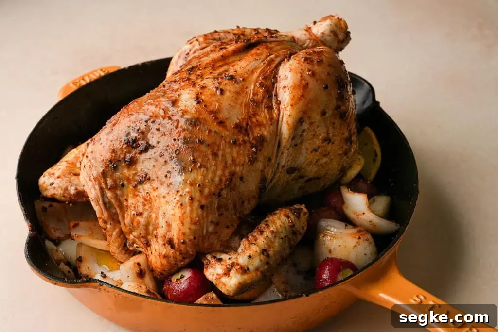 a whole chicken prepped for the oven, in a yellow skillet with diced vegetables