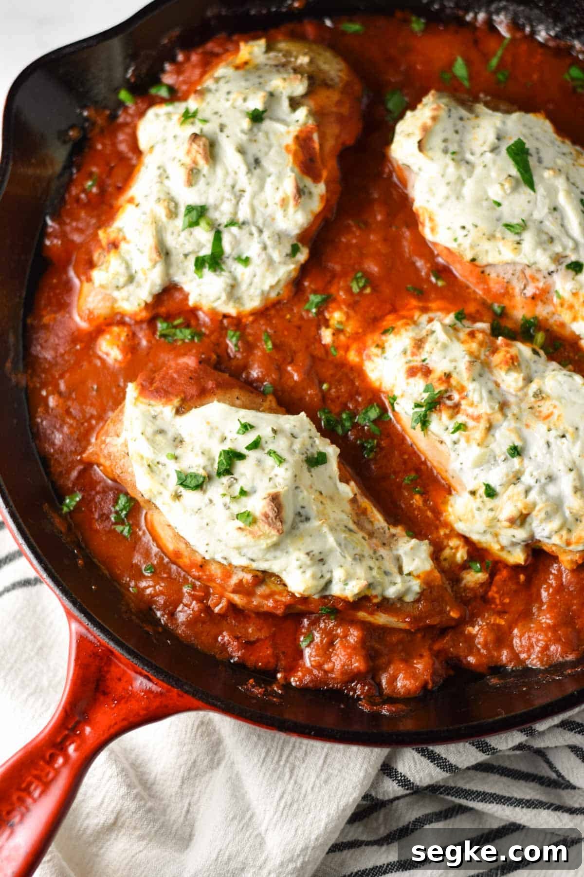 A red pan with chicken breasts topped with ricotta cheese and parsley.