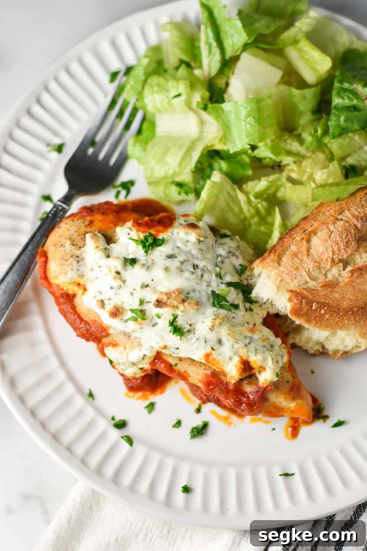 Ricotta chicken on a plate with a Caesar salad and bread.