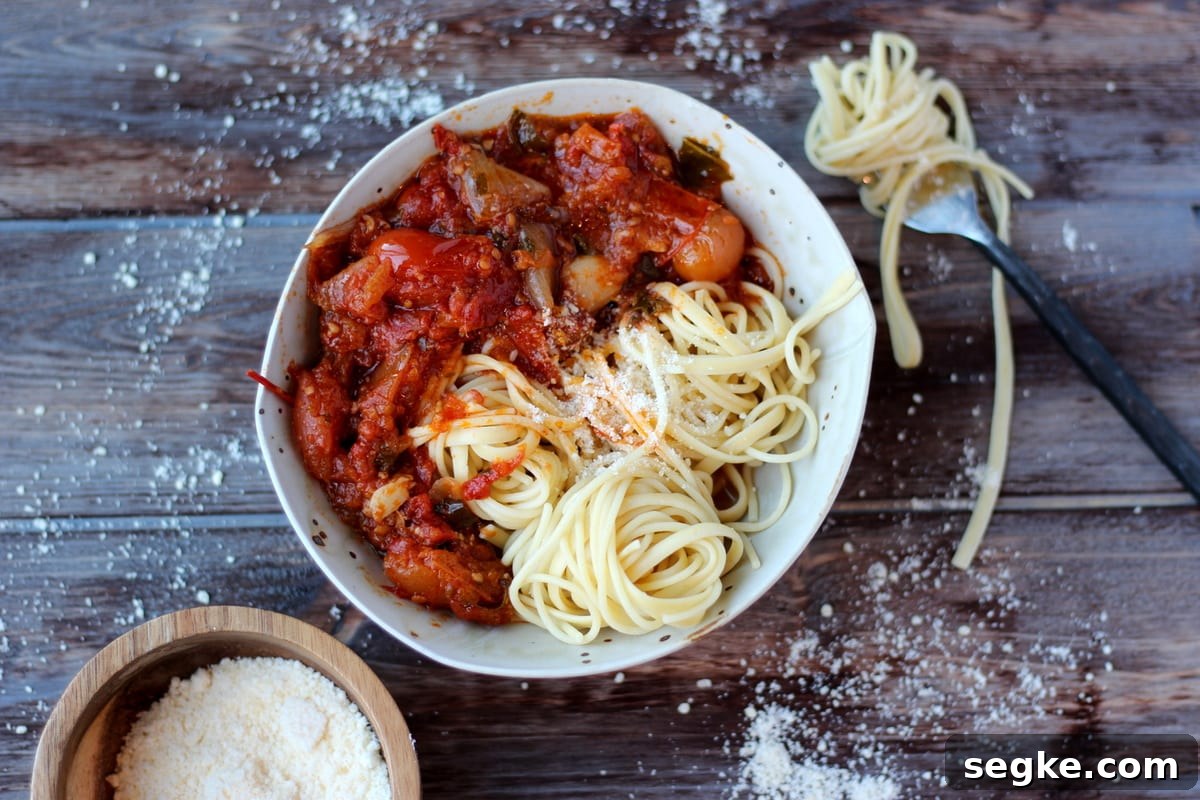 Roasted tomato sauce in a bowl with spaghetti noodles and grated parmesan cheese next to a bowl of cheese and a fork wrapped in noodles.