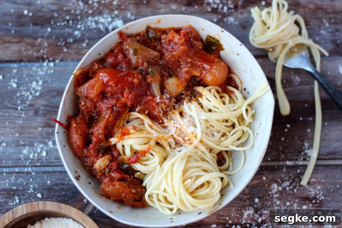 A bowl full of spaghetti noodles and roasted tomato sauce with a sprinkling of grated parmesan cheese.