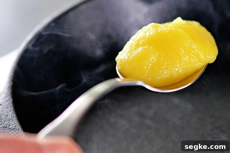A spoon filled with ghee is on top of a smoking hot cast iron skillet.