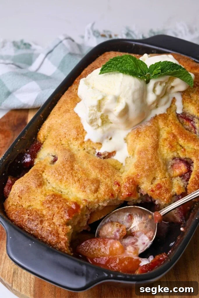 A black baking dish filled with sourdough peach cobbler topped with vanilla ice cream.